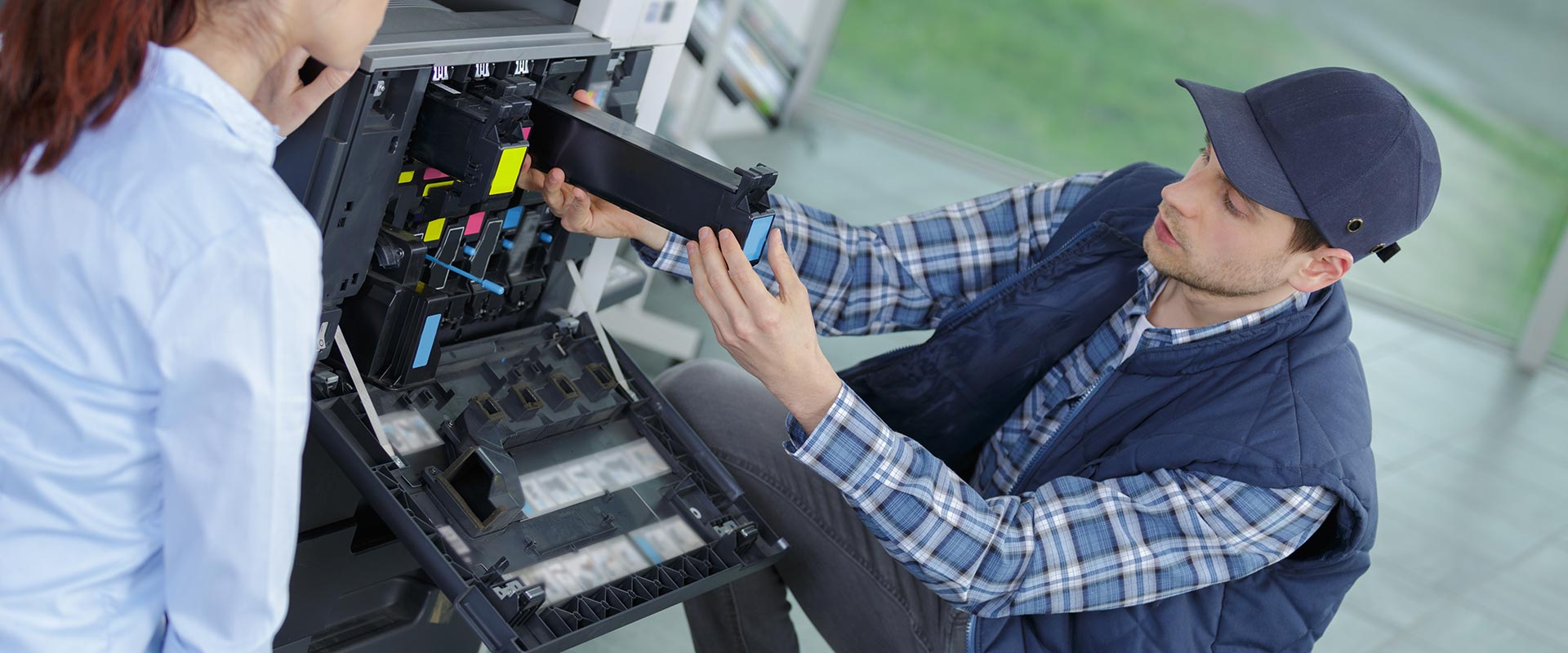 A technician dressed in blue demonstrating a office worker how to install toner cartridges.